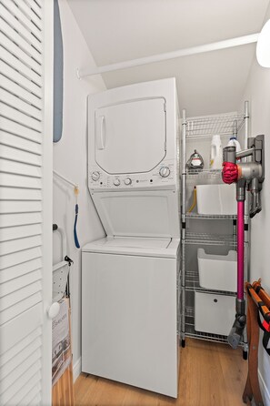 A compact laundry room with a front-loading washing machine, a drying rack, and a hose for water connection. - Venice Beach 1-Bedroom Apartment w/ Roof Top Deck (Los Angeles)