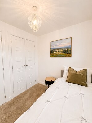 A bedroom with a bed, a nightstand, a chandelier, a door, and a painting on the wall. - Modern 3-Bed Home Free Driveway Parking, Fast Wi-Fi (Ebbsfleet Valley)
