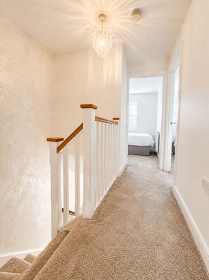 A carpeted staircase with white railings and a chandelier. - Modern 3-Bed Home Free Driveway Parking, Fast Wi-Fi (Ebbsfleet Valley)