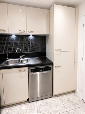 A modern kitchen with a stainless steel dishwasher, a black tiled backsplash, and white cabinetry. - Modern 3-Bed Home Free Driveway Parking, Fast Wi-Fi (Ebbsfleet Valley)
