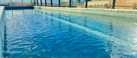 A swimming pool with clear blue water and a view of the sky and buildings in the background.