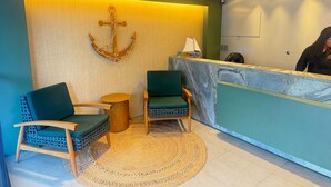 A reception area with a marble counter, two green chairs, a woven rug, and a wooden anchor decoration. - Season Smart Flats By Flat na Praia (Ipojuca)