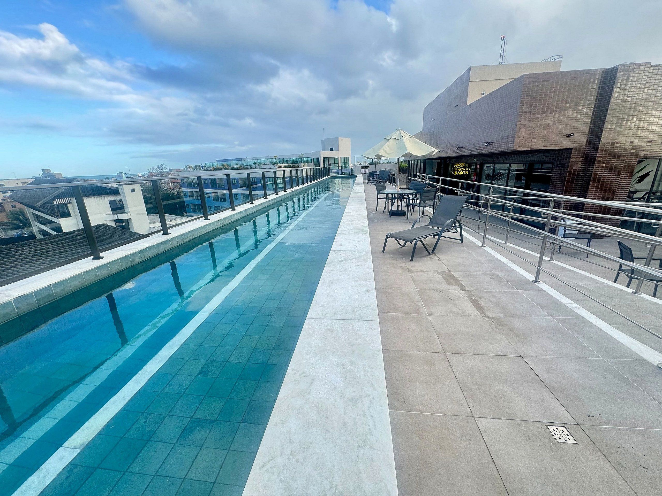 Un espace piscine aménagé sur le toit, offrant une vue dégagée sur le paysage urbain, un coin salon avec des tables et des chaises, et un bâtiment moderne doté d’une façade en verre.