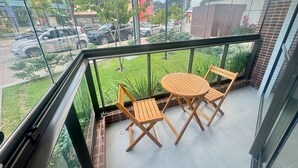 A balcony with a table and chairs, overlooking a street with parked cars and buildings. - Season Smart Flats By Flat na Praia (Ipojuca)