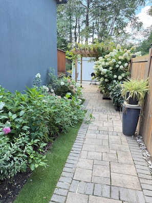 Un chemin de jardin pavé qui mène à une pergola en bois couverte de plantes grimpantes.