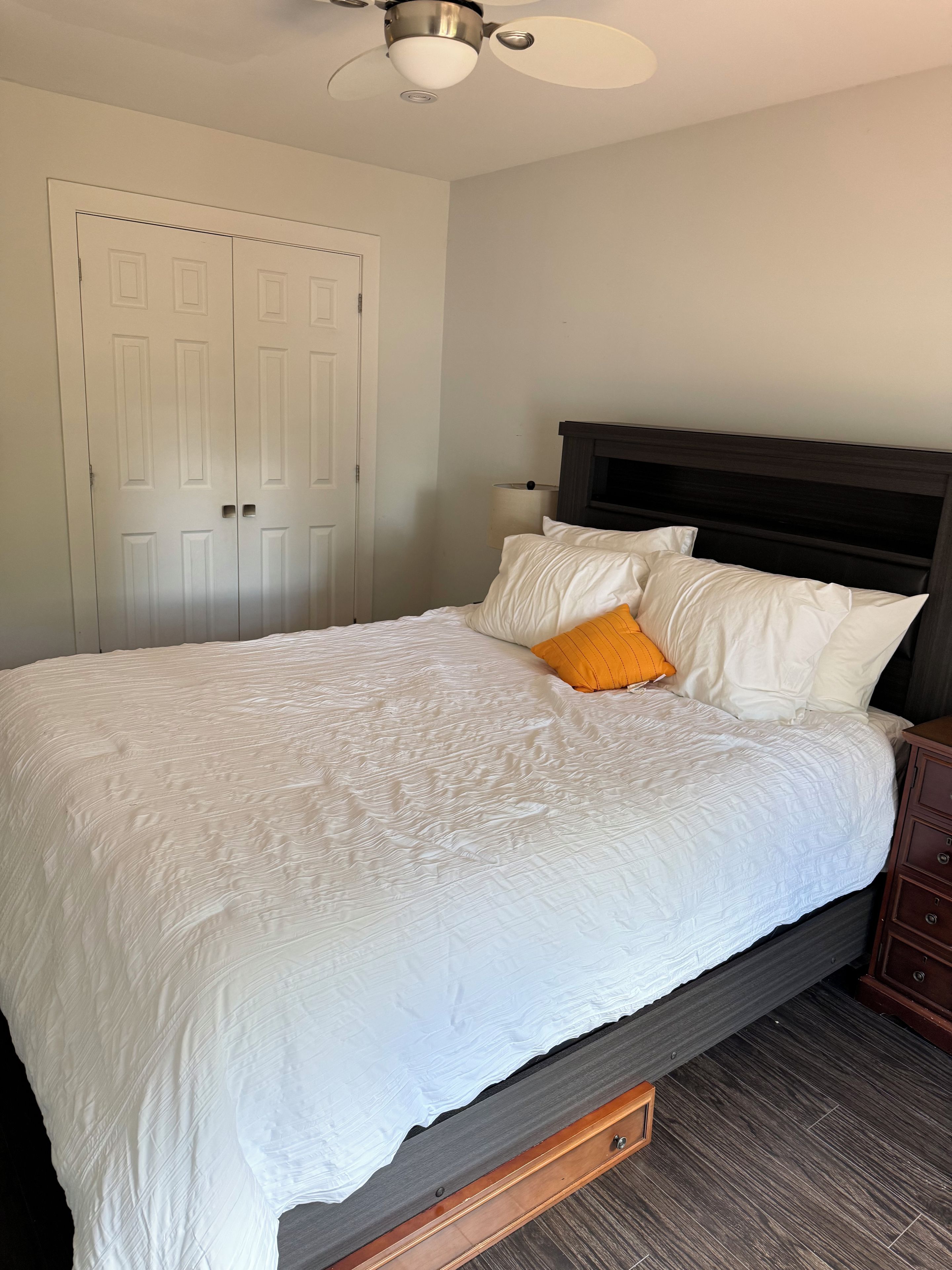 A bedroom with a bed, a nightstand, a ceiling fan, and a door.