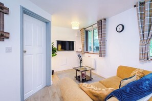 Una sala de estar con un sofá, una mesa de centro, un televisor y una ventana con cortinas.