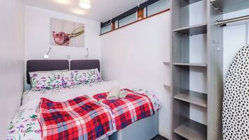 A bedroom with a bed, a wardrobe, and a wall-mounted shelf.