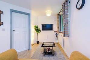 Un salon avec un téléviseur, une petite table, une plante en pot et une porte.