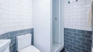 A bathroom with white and grey tiles, a glass shower enclosure, and a white toilet. - Cosy 1-Bed Apartment Wigan | Free Parking (Greater Manchester)