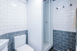 A bathroom with white and grey tiles, a glass shower enclosure, and a white toilet. - Cosy 1-Bed Apartment Wigan | Free Parking (Greater Manchester)