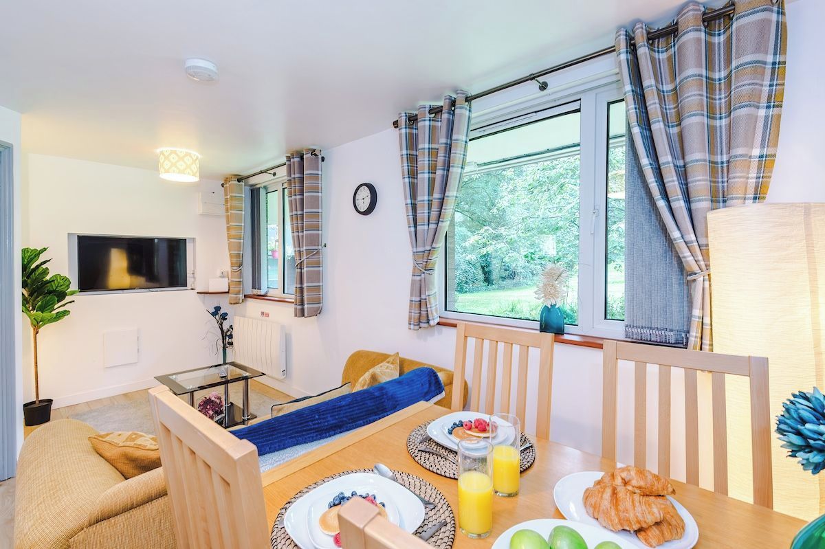 A cozy room with a bed, a dining table with breakfast, a TV, and a window with curtains.