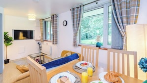 A cozy room with a bed, a dining table with breakfast, a TV, and a window with curtains. - Cosy 1-Bed Apartment Wigan | Free Parking (Greater Manchester)