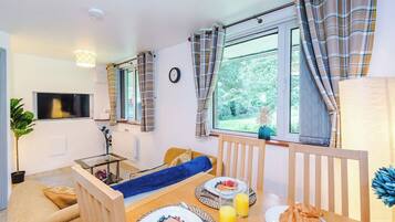 A cozy room with a bed, a dining table with breakfast, a TV, and a window with curtains.