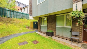 A residential building with a paved driveway, a green fence, and a small garden area. - Cosy 1-Bed Apartment Wigan | Free Parking (Greater Manchester)