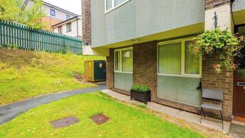 A residential building with a paved driveway, a green fence, and a small garden area.