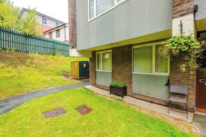 A residential building with a paved driveway, a green fence, and a small garden area. - Cosy 1-Bed Apartment Wigan | Free Parking (Greater Manchester)