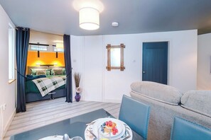 A room with a bed, a dining table with breakfast, a sofa, and a door.