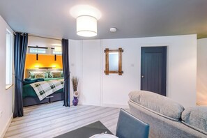 Una habitación compacta con cama, sofá, una mesita y un espejo en la pared.