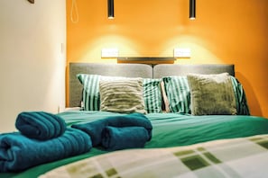A bed with green bedding and striped pillows, a headboard with a light fixture, and a wall with a warm color tone.