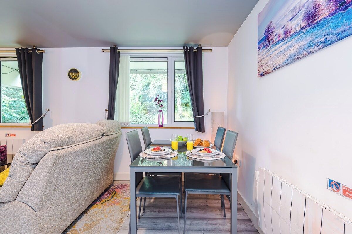 Un coin repas avec une table dressée pour deux personnes, un canapé et une fenêtre avec des rideaux.