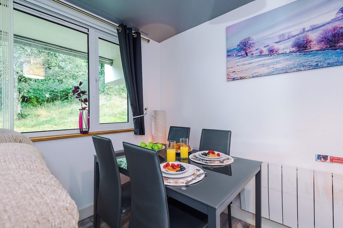 Un comedor con una mesa dispuesta para dos personas, fruta y jugo sobre la mesa, y un cuadro en la pared.