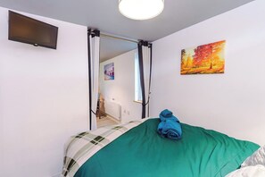 Una habitación con una cama, un cuadro, un televisor y vistas a otra habitación.