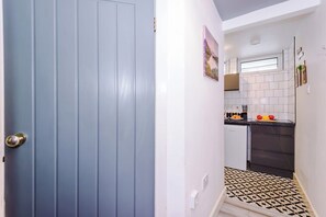 Un pasillo estrecho que conduce a una cocina con salpicadero de azulejos y una puerta con picaporte plateado.