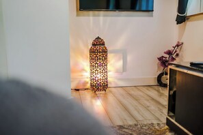 Una habitación con una lámpara de pie con estampado, un televisor montado en la pared y una planta en el suelo.