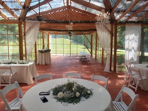 A covered outdoor event space with tables and chairs, a chandelier, and a view of a green landscape.