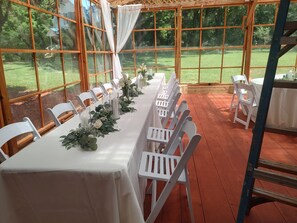 A covered outdoor dining area with tables and chairs, large windows, and a view of the outdoors.