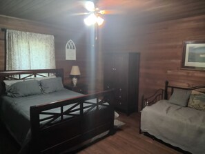 A room with a wooden bed, a nightstand with a lamp, a ceiling fan, and a framed picture on the wall.