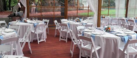 Un espace extérieur aménagé pour les événements, avec des tables rondes, des chaises blanches et des ventilateurs de plafond.