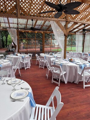 An outdoor event space with round tables, white chairs, and ceiling fans.