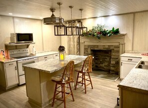 A kitchen with a central island, wooden chairs, a microwave, stove, and a fireplace.