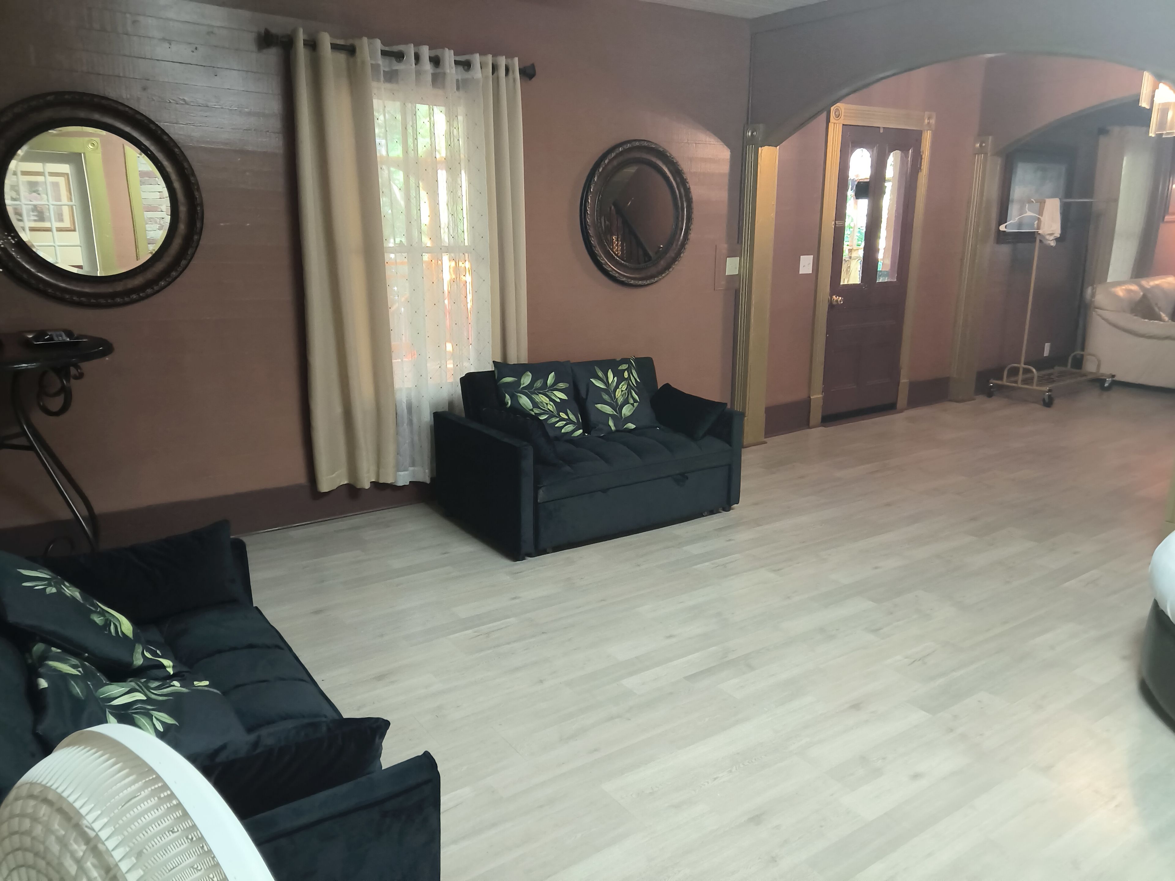 Un salon avec un canapé, un miroir rond et une fenêtre avec des rideaux.