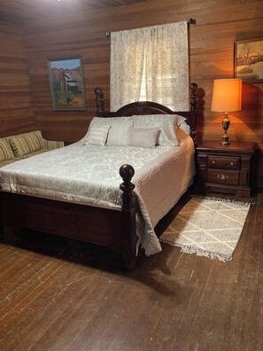 A wooden-paneled room with a bed, a nightstand, a lamp, and a painting on the wall.