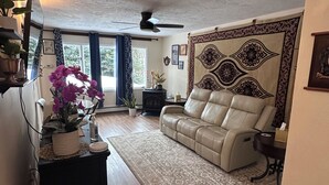 Ein Wohnzimmer mit einer Ledersofa, einem gemusterten Teppich, einem Deckenventilator und einer Wand mit Dekorationselementen.