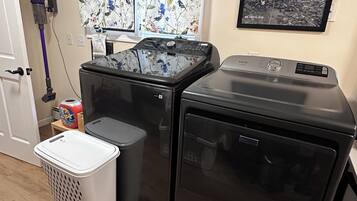 A laundry room with two washing machines, a dryer, a vacuum cleaner, and a laundry basket.
