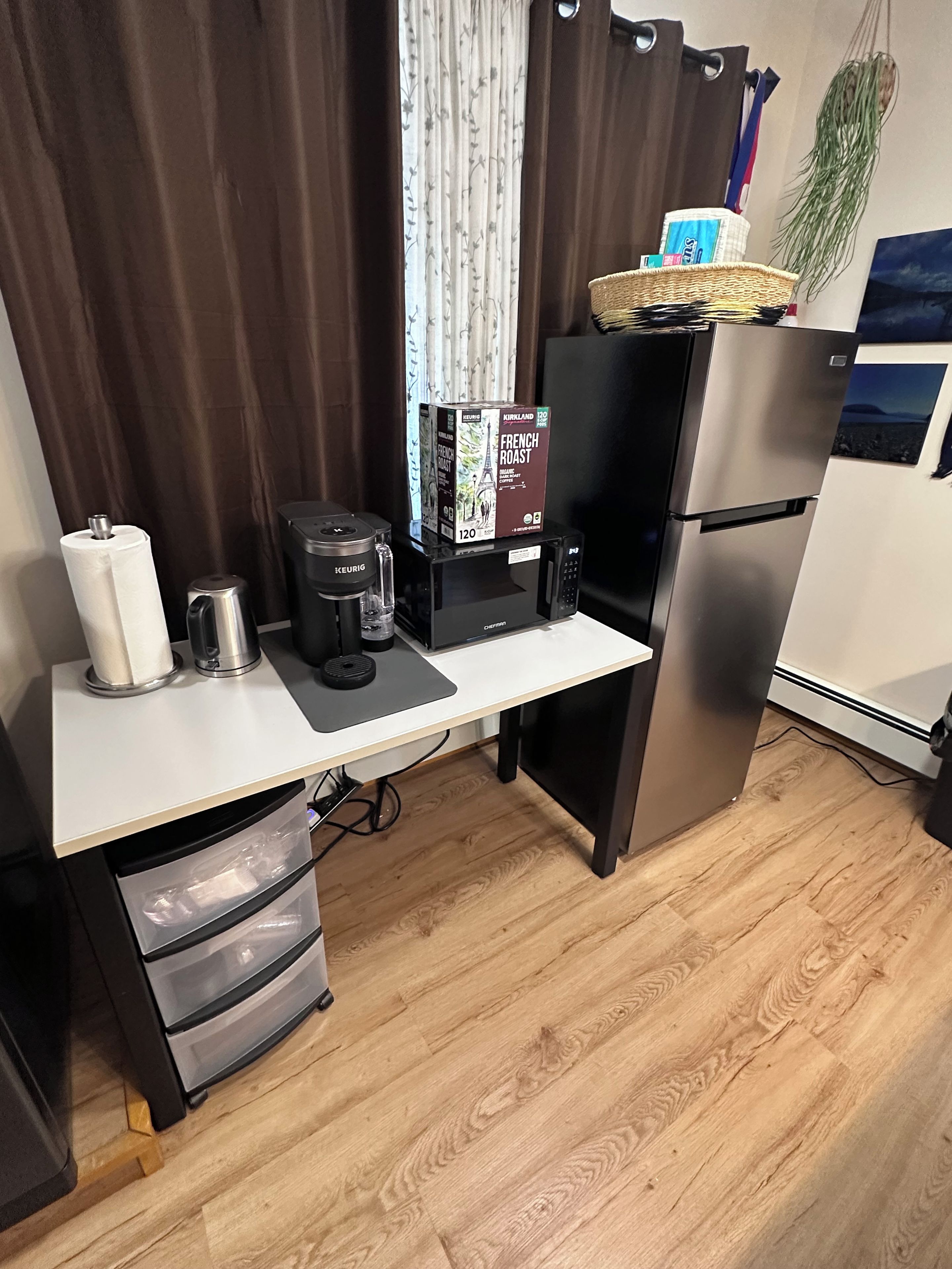 Une petite cuisine équipée comprenant un réfrigérateur en acier inoxydable, une machine à café, un four à micro-ondes et une petite poubelle.