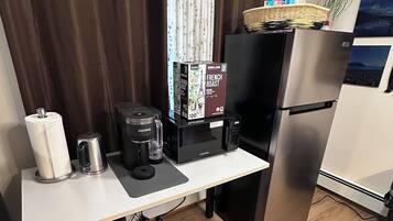A compact kitchenette with a stainless steel refrigerator, a coffee maker, a microwave, and a small trash bin.