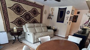 Ein Essbereich mit einem runden Tisch und Stühlen, einer Couch, einem Deckenventilator und einer Wanderausstattung mit Muster.