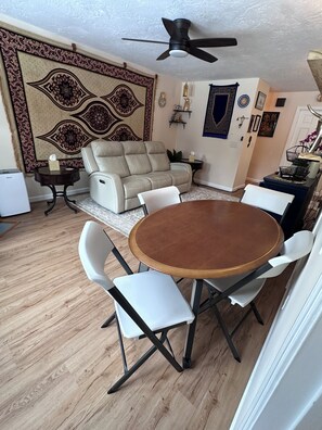 Un coin repas avec une table ronde et des chaises, un canapé, un ventilateur de plafond et une tapisserie à motifs accrochée au mur.