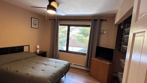 Ein Schlafzimmer mit einem Bett, einem Deckenventilator, einem Fenster mit Vorhängen, einem Fernseher und einem Holzschrank.