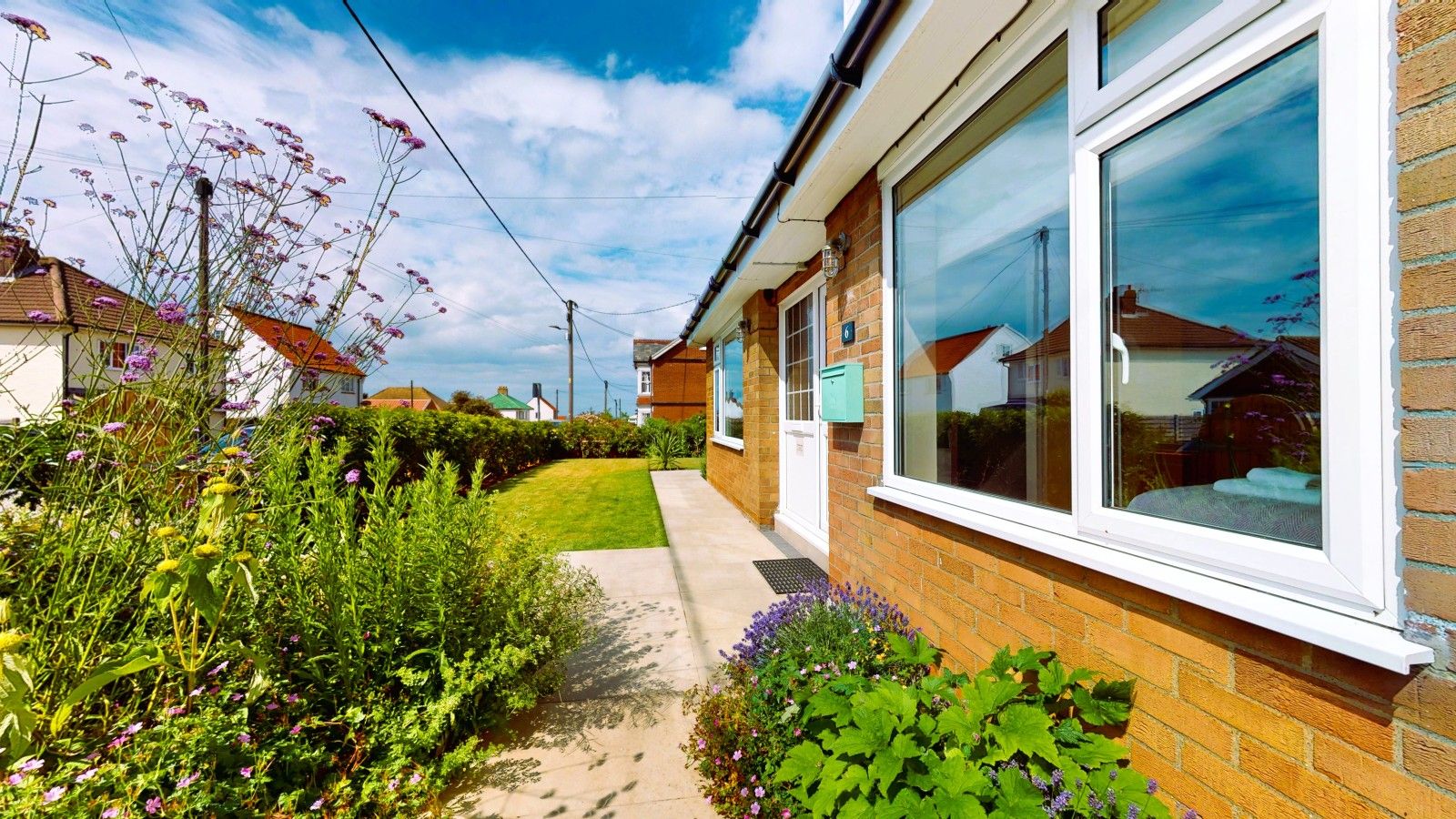 A residential property with a brick exterior, a paved pathway, and a variety of flowering plants.