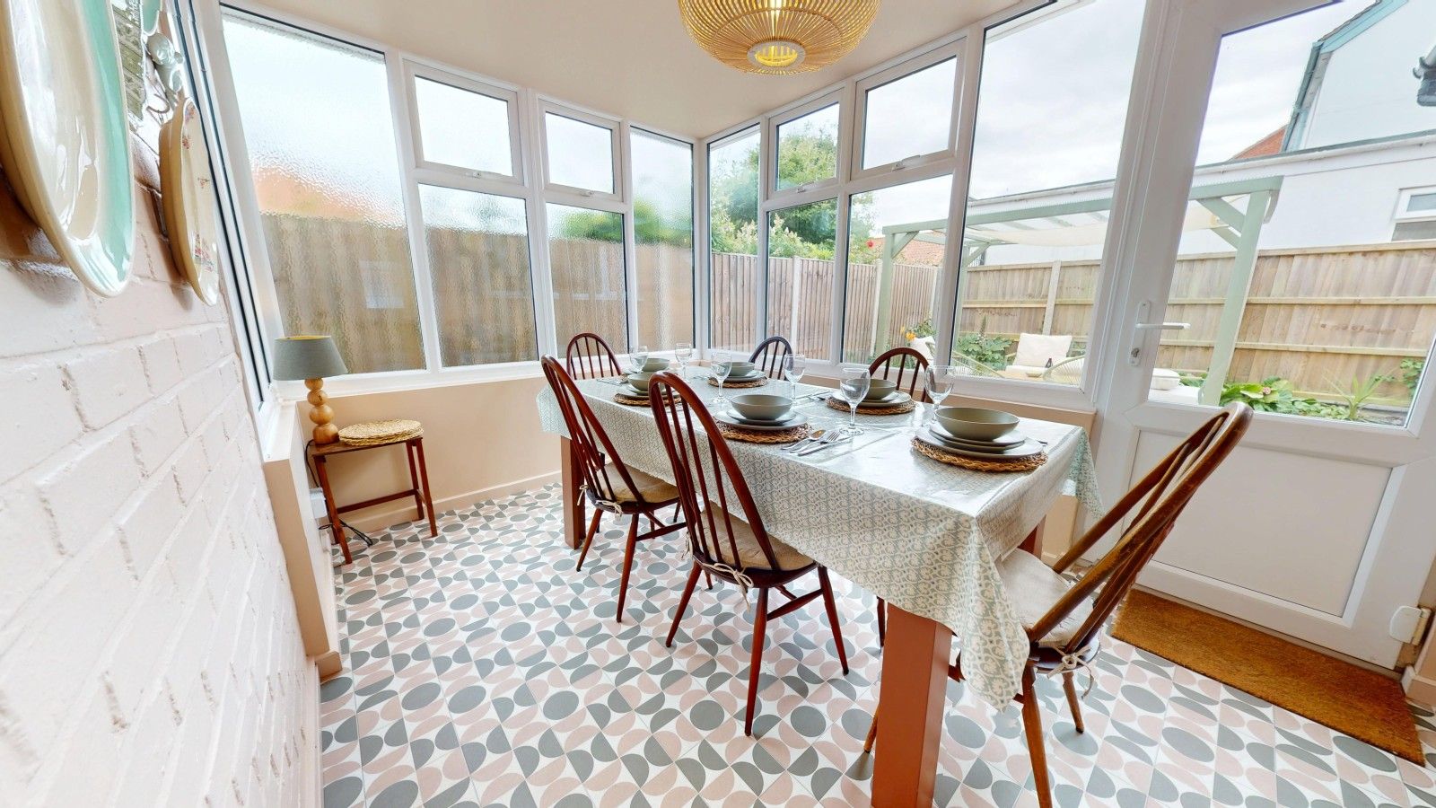 A dining area with a table set for six, surrounded by chairs, large windows, and a patterned floor.