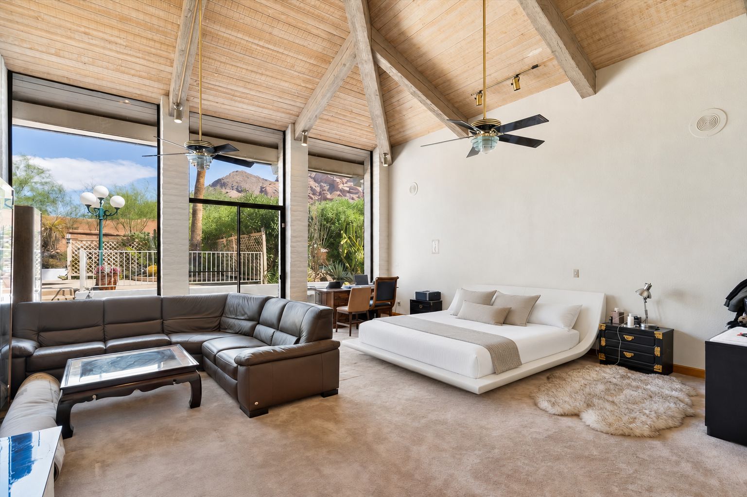 A spacious living area with a large sofa, a bed, and a desk. There are large windows offering a view of the outdoors.