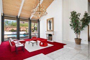 A spacious living room with a red carpet, a fireplace, and a large window overlooking a pool. - 4-bedroom estate with 25 foot ceilings, formal salon and resort-style pool (Paradise Valley)