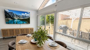 A dining area with a wooden table set for six, surrounded by chairs, with a large window providing a view of the outdoors. - Spacious 5-bedroom house in terrific Cypress with BBQ (Cypress)
