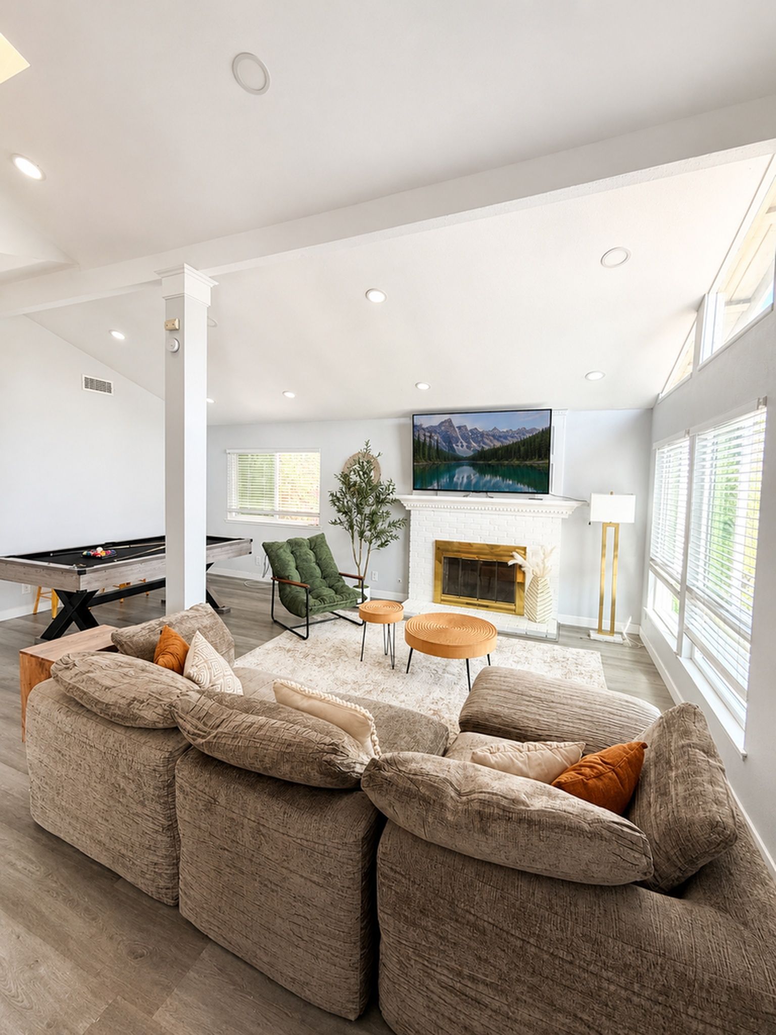 A modern living room with a sectional sofa, a flat-screen TV mounted above a fireplace, and a pool table.